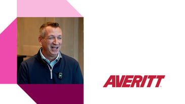 Person in a blue pullover and collared shirt standing indoors with wooden paneling, next to the Averitt logo in bold red text and geometric pink and purple accents.