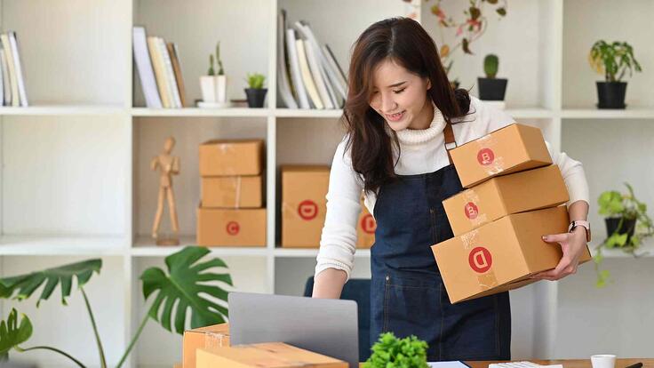 Entrepreneur holding parcels while using laptop