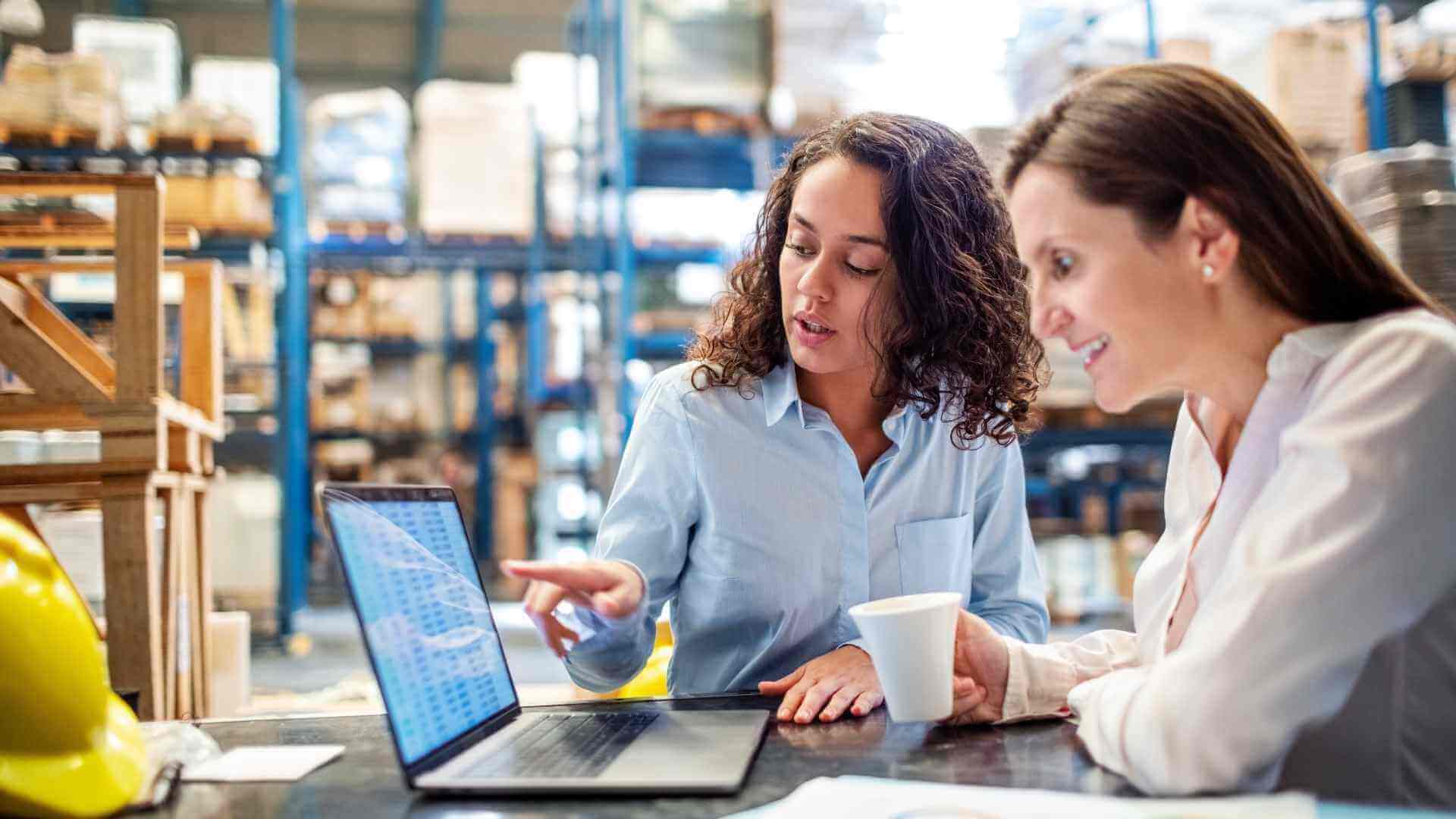 Woman showing inventory on laptop to warehouse manager