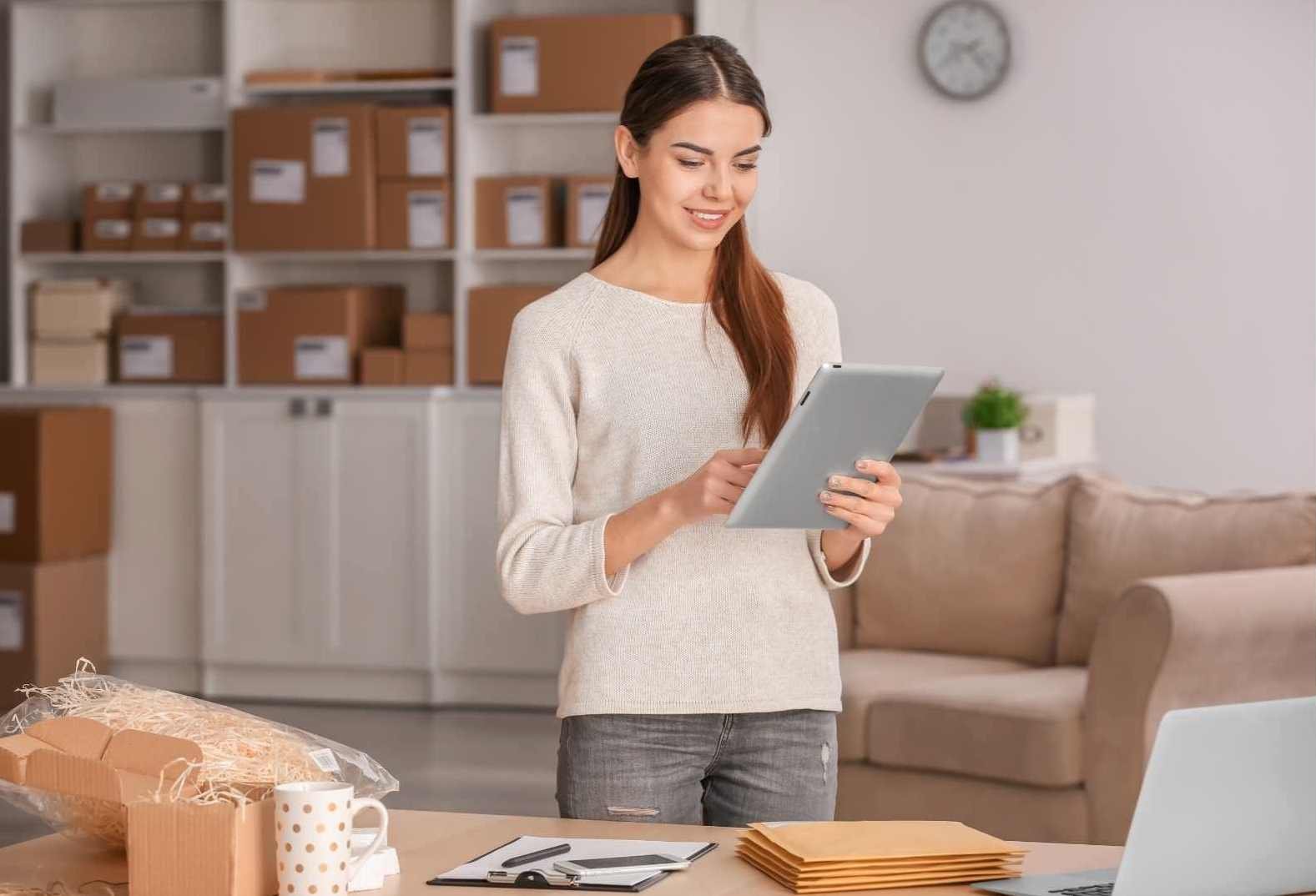 Young Woman with Tablet Preparing Parcel for Shipment to Client