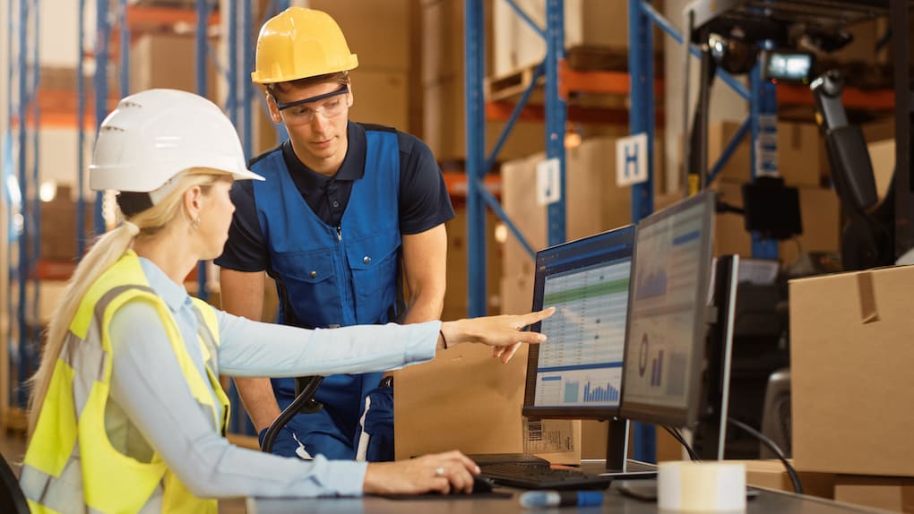 In Retail Warehouse Manager Uses Computer with Inventory Checking Software and Talks with Storehouse Worker about Package Delivery.