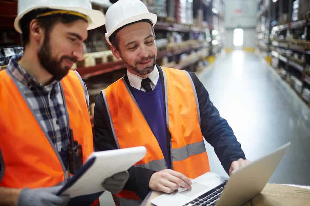 Dispatcher showing warehouse inventory sales in laptop to one of workers